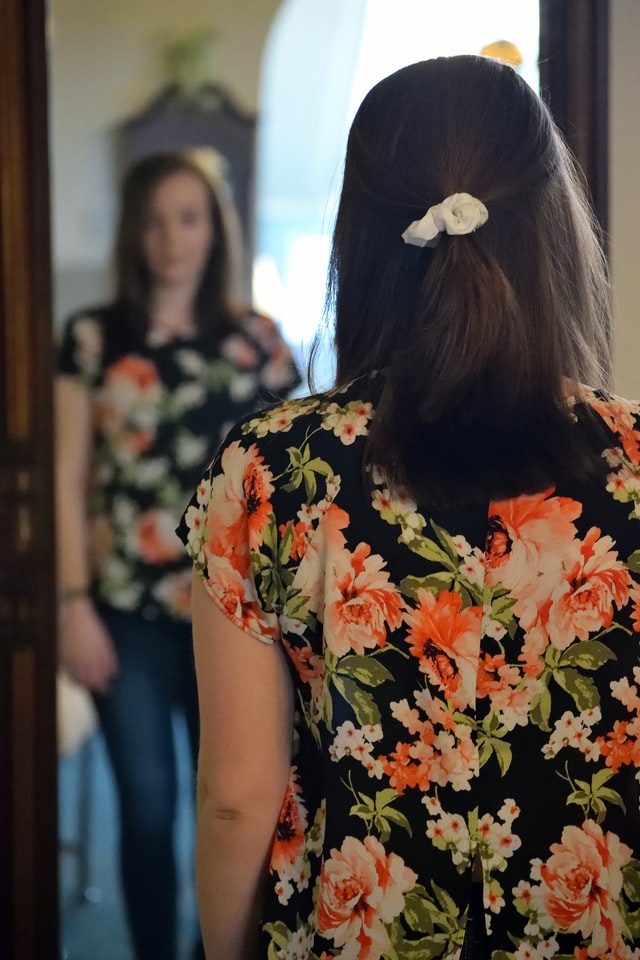 woman in floral dress looking at her reflection in the mirror