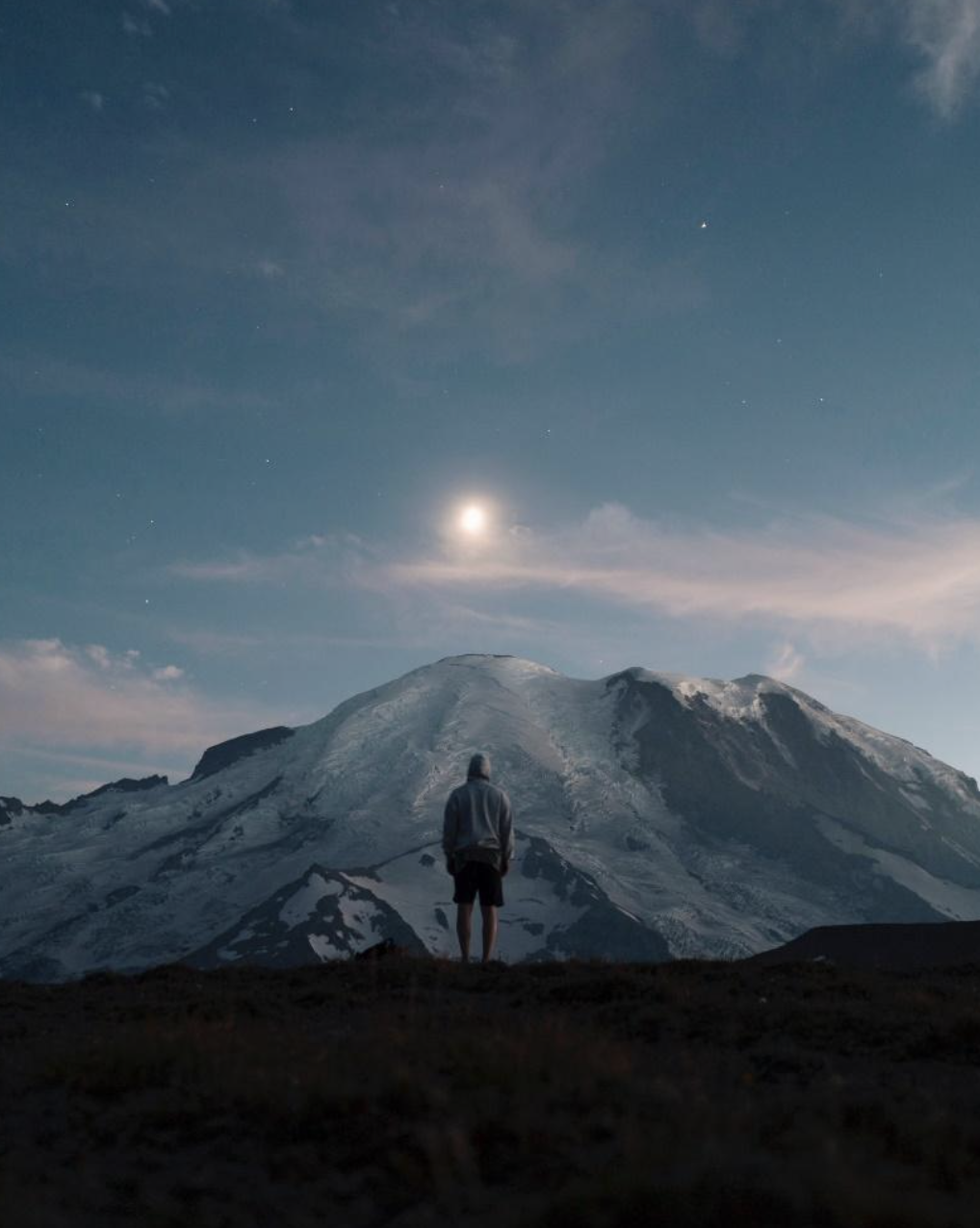 person standing in front of a mountain at sunset staring at it